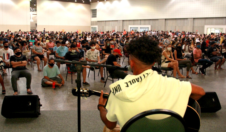 interior do ponto de vacinação no centro de eventos com centenas de jovens sentados em cadeiras enquanto aguardam a vacinação